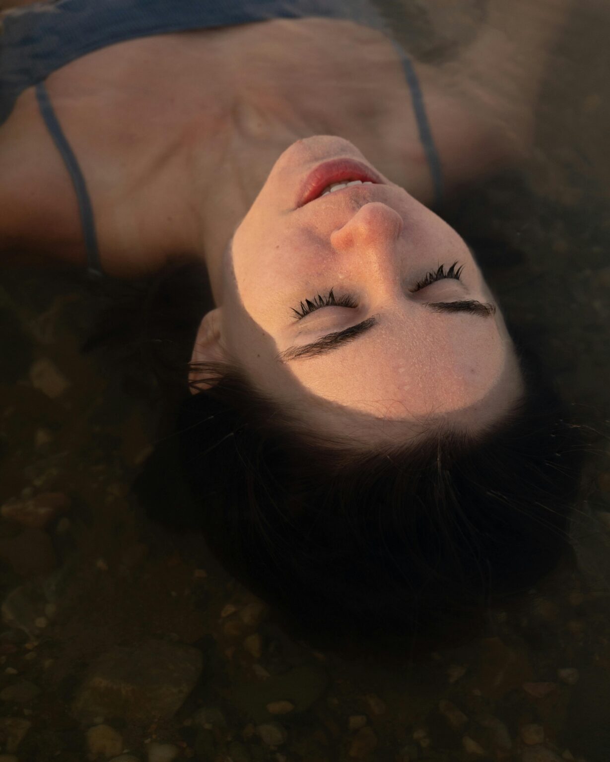 A woman with eyes closed, floating gracefully in tranquil waters, evoking serenity and peace.